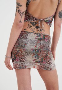 Vestido corto con una mezcla de estampado de leopardo y patrones florales, en tonos de marrón, rojo y verde, con un diseño de lazo en la parte posterior y una textura suave.