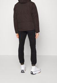 Brown padded jacket with a hood, black jogger pants, and white sneakers featuring black star design on the heel. Simple and modern design.