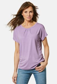Paarse short-sleeve top met een ronde hals en geplooide details. Zachte stof met een gladde textuur. Gecombineerd met strakke blauwe jeans.