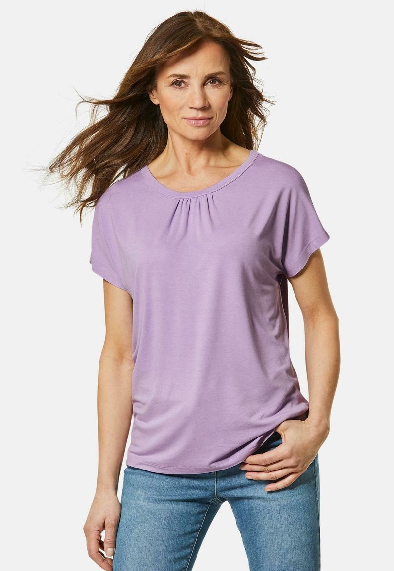 Paarse short-sleeve top met een ronde hals en geplooide details. Zachte stof met een gladde textuur. Gecombineerd met strakke blauwe jeans.