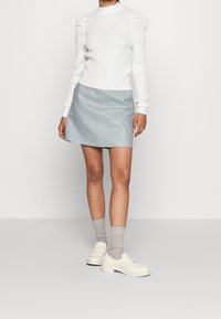 Pull en maille blanche à col montant, associé à une mini-jupe en cuir bleu clair. Des chaussettes gris clair et des chaussures crème épaisses complètent la tenue.