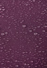 Fioletowy materiał o teksturowanej powierzchni, na którym widać krople wody o różnych rozmiarach, odbijające światło i tworzące wzór kropelek wilgoci.