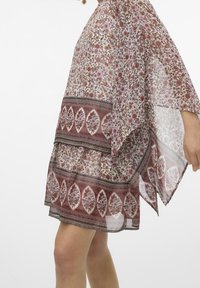 Tunique transparente avec un motif floral dans des nuances de rouge et de rose, présentant un design en étages et des bordures décoratives dans des couleurs contrastées.