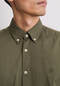 Olijfgroene button-up shirt van gestructureerde stof. Bevat beige knopen en geborduurd logo op de borst. Tailored kraagontwerp.