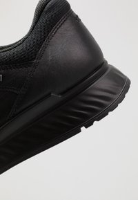 Primo piano del tallone di una sneaker nera che mostra pelle liscia, tessuto a rete e suola spessa e testurizzata con motivo del battistrada.