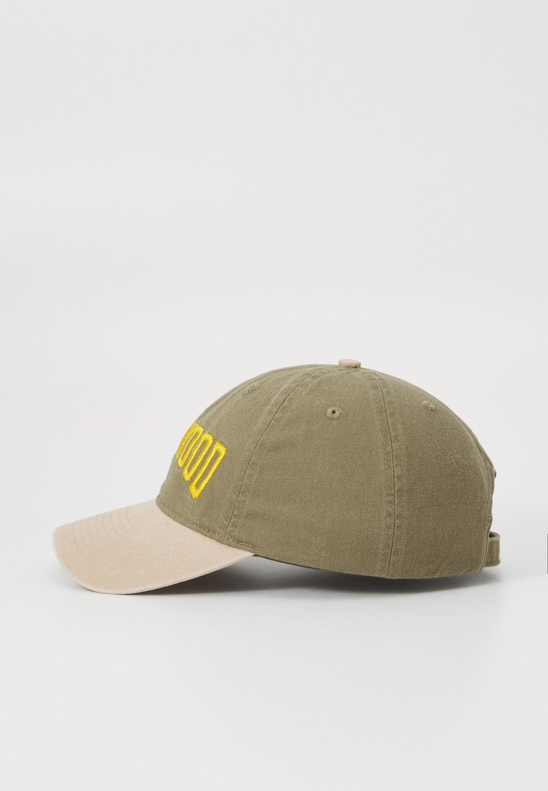 Gorra de béisbol verde oliva con visera beige, que lleva texto bordado amarillo en la parte frontal y una superficie de tela texturizada.