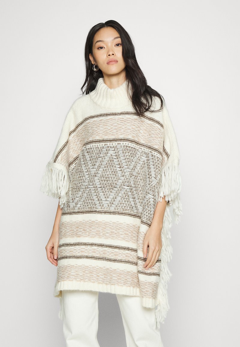 Poncho de malha com gola alta, apresentando riscas horizontais alternadas em bege e branco, padrões de diamante e franjas nos mangas.