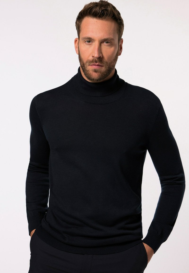 Marineblauer Rollkragenpullover aus weichem Stoff, mit langen Ärmeln und Rippstrick-Details am Kragen und an den Manschetten, getragen mit Händen in den Taschen.