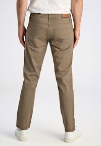 Pantalones de twill de algodón marrón con corte recto; cuentan con dos bolsillos traseros y una etiqueta de cuero color crema en la cinturilla.