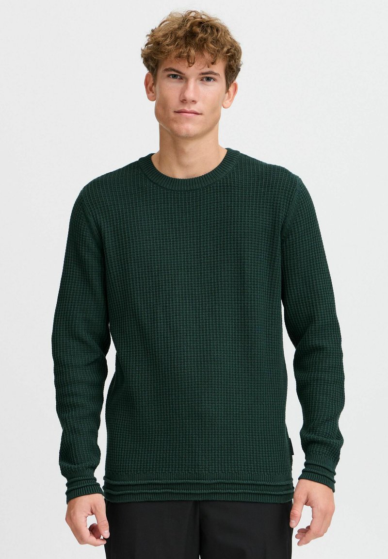 Pull en tricot vert texturé avec des poignets et un ourlet côtelés, doté d'un col rond et d'une coupe ajustée. Le matériau semble tricoté avec un motif.