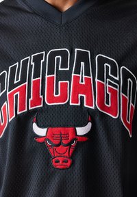 Juodas tinklinis krepšinio marškinėlis su užrašu "CHICAGO" ryškiomis baltomis ir raudonomis raidėmis, o centre yra raudonas išsiuvinėtas buliaus logotipas.