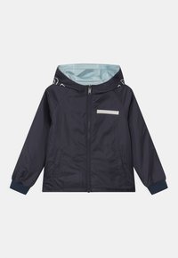 Chaqueta ligera azul marino con capucha, cierre de cremallera, bolsillos laterales y parche reflectante. Cuenta con puños elásticos y un forro en contraste de azul claro.