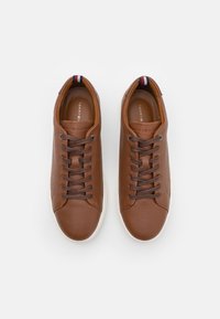 Sneakers in pelle marrone con una superficie testurizzata, dotati di lacci marroni scuri, una suola in gomma bianca e un accento decorativo sul tallone.