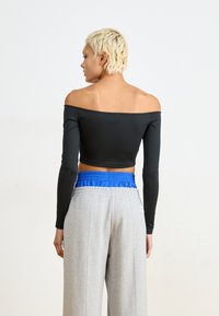 Musta olkaimeton lyhythihainen crop-top, joka on yhdistetty harmaisiin collegehousuihin, joissa on sininen elastinen vyötärö. Sileä kangas, tiukka muotoilu.