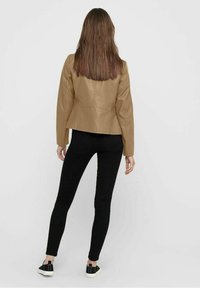 Giacca in ecopelle color beige con un design aderente, dettagli sulle cuciture posteriori, abbinata a jeans skinny neri e sneakers nere.