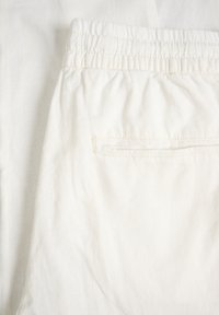 Baltos spalvos lininė medžiaga su elastine liemens juosta ir viena kišene gale su siūtu atidarymu. Audinio tekstūra atrodo minkšta ir lengva.