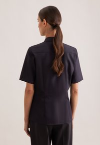 Koszula z krótkim rękawem i kołnierzykiem w ciemnogranatowym materiale. Posiada dopasowany krój, gładką fakturę i minimalistyczny design.