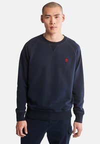 Sweatshirt navy con maniche lunghe, polsini e orlo a coste, e un piccolo logo rosso sul petto. Realizzato in tessuto morbido e strutturato.