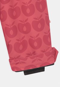 Tecido vermelho com um padrão de maçãs repetido em uma tonalidade mais escura. A barra tem um detalhe elástico preto franzido para um acabamento ajustado.