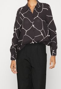 Chemise noire à boutons avec un motif abstrait blanc, à manches longues et col classique, associée à un pantalon noir taille haute.