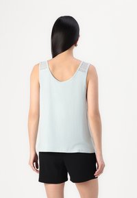 Haut sans manches bleu clair avec un dos en forme de goutte, présentant des accents en dentelle sur les épaules et un tissu lisse. Associé à un short noir.