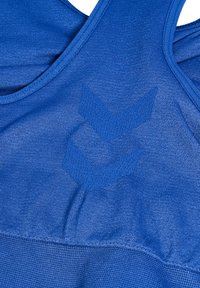 Top de deporte azul sin mangas que presenta una textura suave, un diseño de espalda nadadora y un sutil patrón de logotipos integrado en la tela.