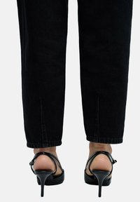 Sandalias de tacón alto negras con abertura en la parte trasera, con parte superior de cuero suave y tacón delgado, combinadas con jeans negros hasta los tobillos.
