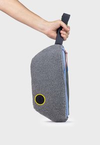 Bolsa de tela gris con un exterior de forro polar texturizado y cremallera azul, que presenta un acento circular amarillo y un asa negra robusta.