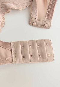 Beige melltartó rész puha anyagból, fodros élekkel és kapcsos zárással; állítható pánttal és mintázott szalag részletekkel rendelkezik.