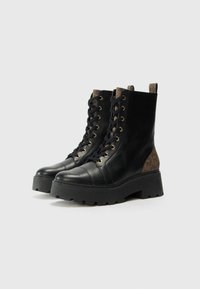 Mustad musta nööriga ankle saapad, millel on sile naha viimistlus, paks must tald ja pruuni mustriga aksent kontsal. Kuldsete aukude detail.
