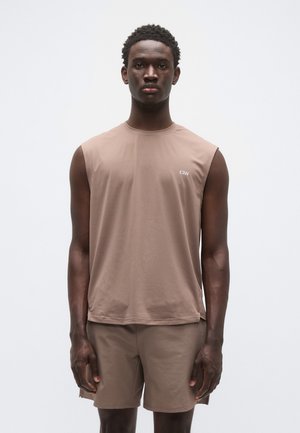 Gaiši brūna bezpiedurkņu sporta krekls ar apaļu kakla izgriezumu un fakturētu audumu, kombinēts ar atbilstošiem šortiem. Minimālistisks logotipa uzraksts.