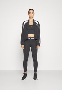Black athletic outfit including a cropped jacket with white accents, a fitted crop top, high-waisted leggings, and black athletic shoes.