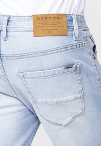 Jeans de denim de lavado claro con un corte recto, que cuentan con una etiqueta de marca de cuero en la cintura trasera y un solo bolsillo trasero con detalles de costura.
