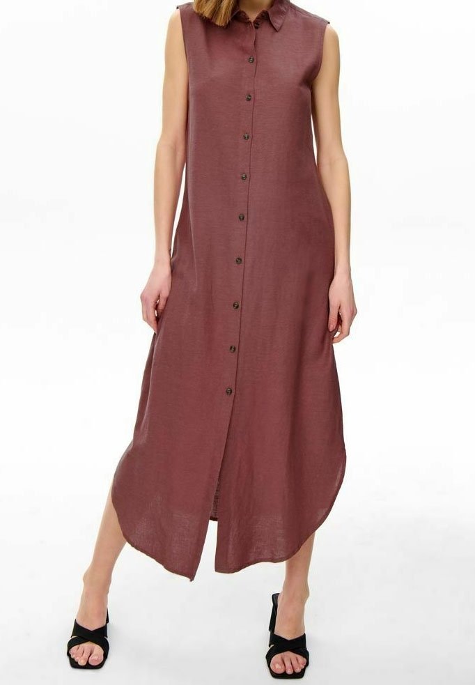 Robe midi marron sans manches à boutons avec col, portée avec des sandales noires à talons sur fond blanc.