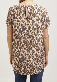 Haut à manches courtes imprimé léopard, avec une découpe en forme de goutte à l'arrière. Couleurs beige, gris, marron et accents dorés.