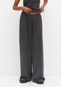 Kolvgrå vida byxor i mjukt ribbat material med resårmidja och justerbar dragsko, i kombination med bruna slip-ins.