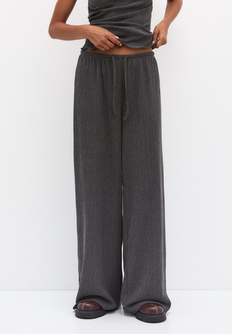 Kolvgrå vida byxor i mjukt ribbat material med resårmidja och justerbar dragsko, i kombination med bruna slip-ins.