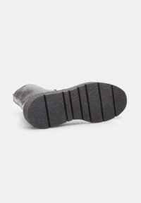 Semelle de botte en caoutchouc noir avec une surface texturée et adhérente, présentant de profonds sillons pour une meilleure traction et une forme arrondie au niveau du talon.