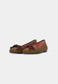 Des ballerines en daim marron avec un bout arrondi, présentant un accent en corde nouée à l'avant et une doublure intérieure lisse de couleur rouge contrastante.