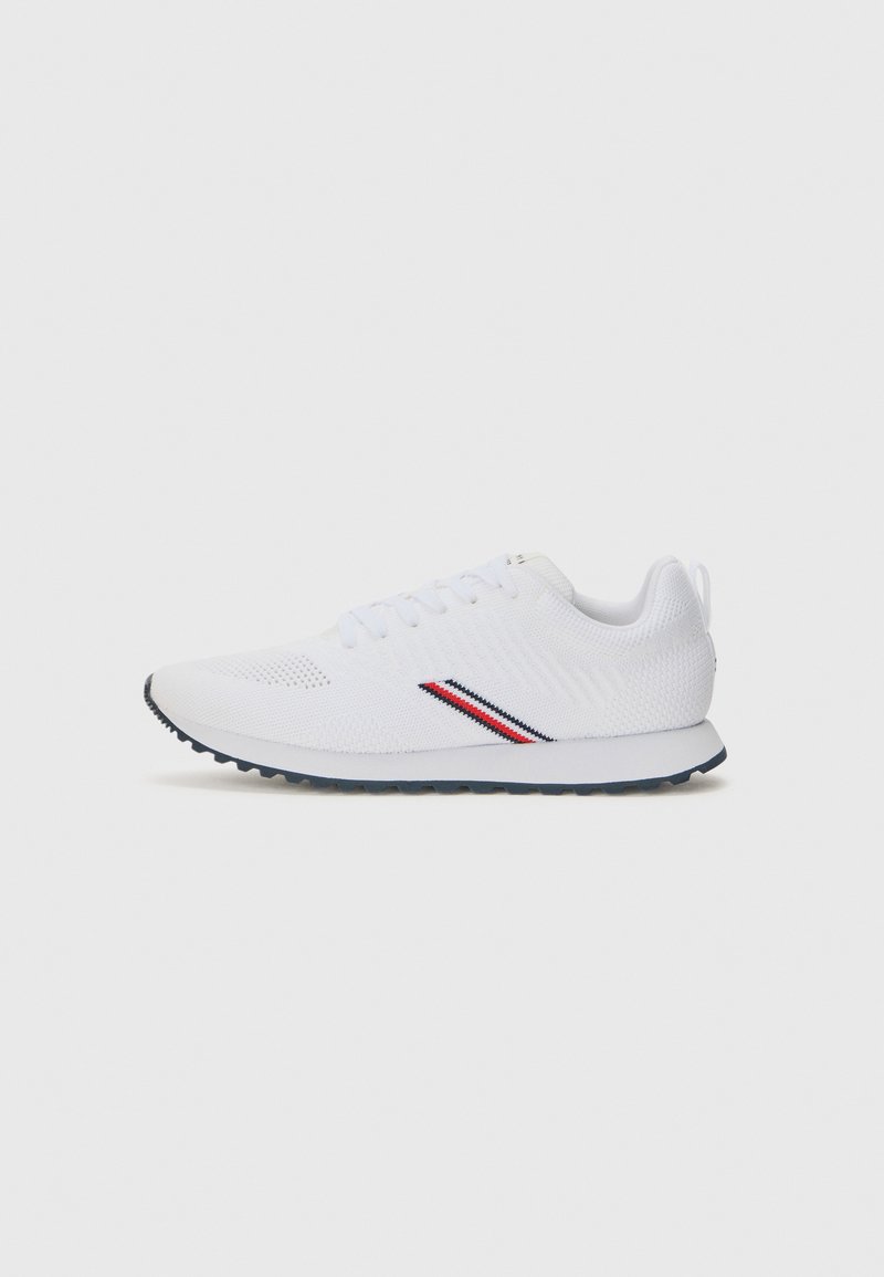 Scarpe da ginnastica bianche con una tomaia in maglia testurizzata, con dettagli a strisce rosse e blu sui lati e suola in gomma nera.