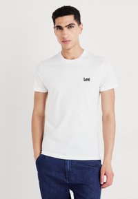 T-shirt blanc à manches courtes en coton avec un col rond, arborant un petit logo noir "Lee" sur le côté gauche de la poitrine.