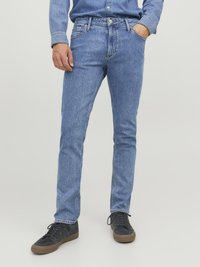 Jeans de mezclilla azul claro con corte ajustado, diseño clásico de cinco bolsillos y detalles de costura sutiles. Llevados con zapatillas negras.