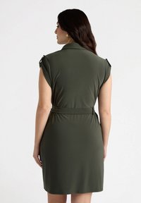 Abito verde oliva con colletto, maniche a farfalla e vita cintura. Tessuto liscio ed elastico con un design semplice e lineare.