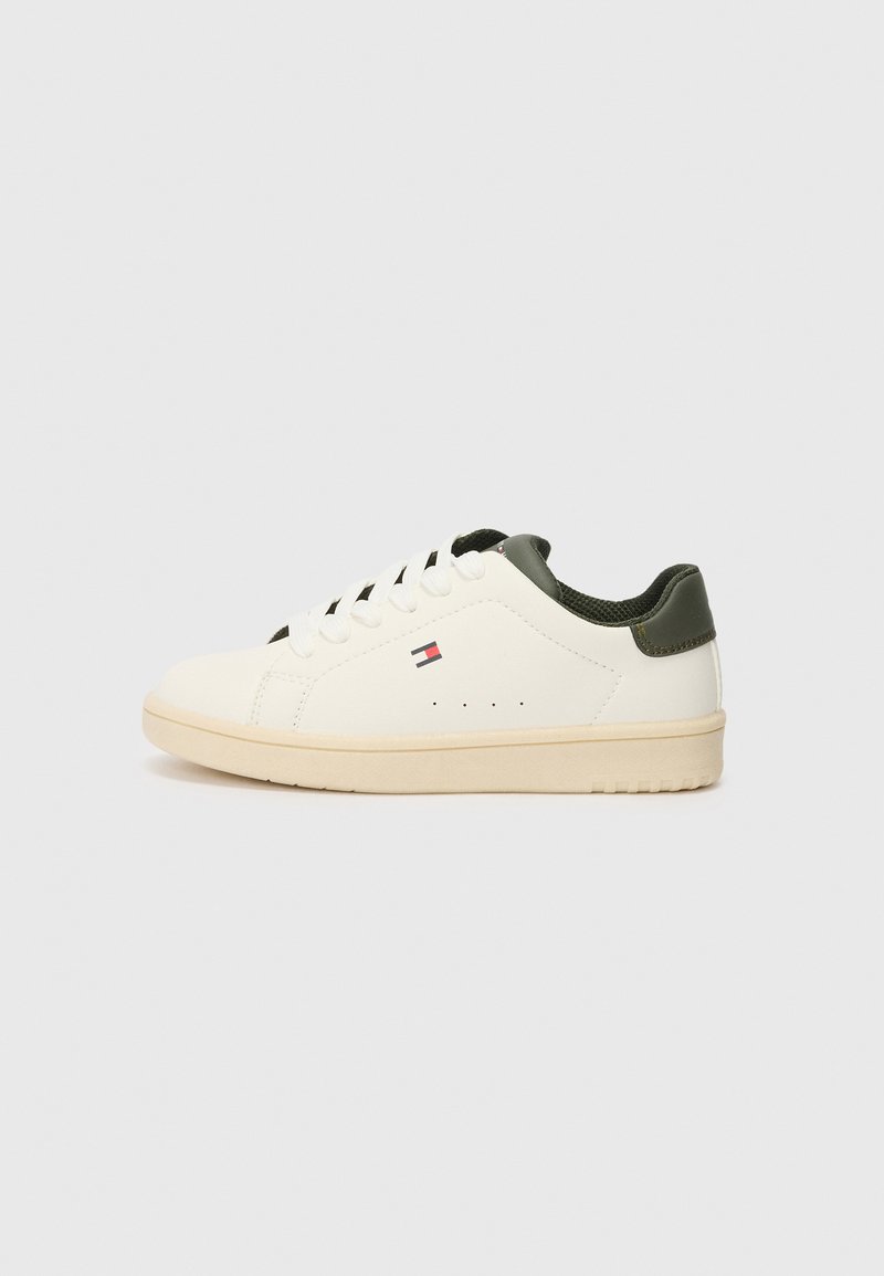 Zapatilla blanca con parte superior de cuero suave, acentos verdes en el talón, cordones redondos y suela de goma texturizada. Presenta detalle del logo en el lado.