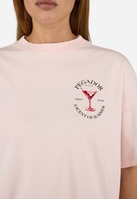Rosa bomull t-skjorte med rund hals og korte ermer. Fronttrykt design av et cocktailglass med tekst rundt.