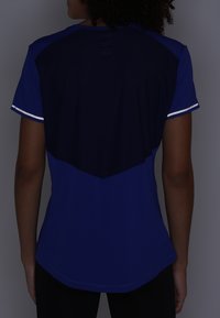 Blå atletisk tröja med en mörk marinblå bakpanel, korta ärmar och reflekterande kantband. Mjuk, lätt och fukttransporterande tyg.