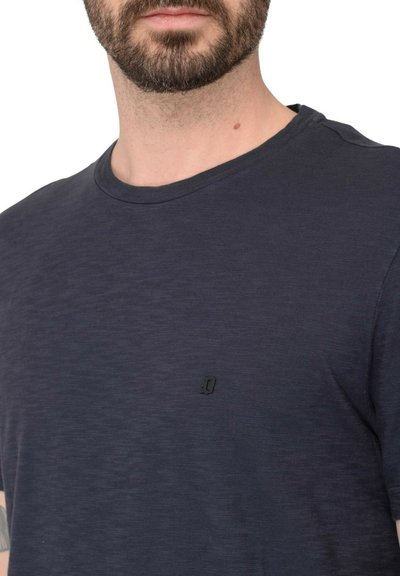 T-shirt di cotone blu navy con colletto rotondo, maniche corte e un piccolo logo nero sul petto. Texture morbida, design semplice.