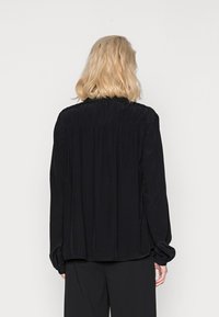 Schwarze Bluse mit langen Ärmeln und gerafften Details am Hals und an den Manschetten, im entspannten Schnitt und mit glatter Textur, von hinten präsentiert.