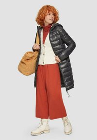 Schwarze Daunenjacke, weißer Strickwesten, roter Rollkragenpullover, rostfarbene weit geschnittene Hose, cremefarbene Stiefel und braune Tasche. Weiche Texturen und abwechslungsreiche Silhouetten.