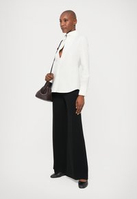 Hvid skjorte med mandarin krave, parret med brede sorte bukser og sorte flade sko. Hun bærer en lille mørk taske.